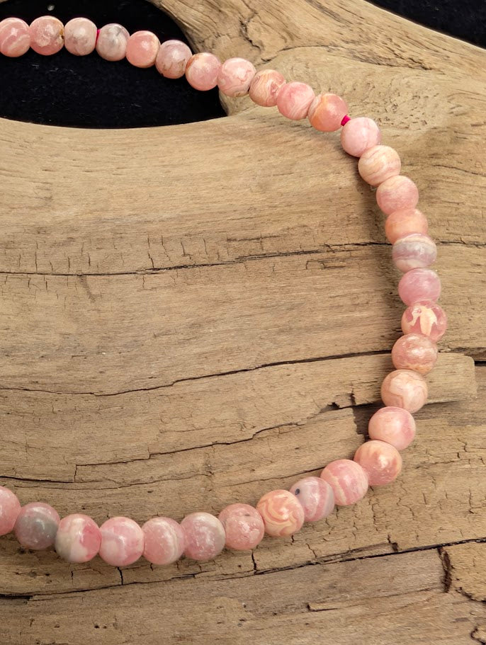 Macro close-up of 4mm A-grade polished Rhodochrosite beads highlighting the high-gloss finish, pink colouration, and heavy natural white calcite intergrowth.