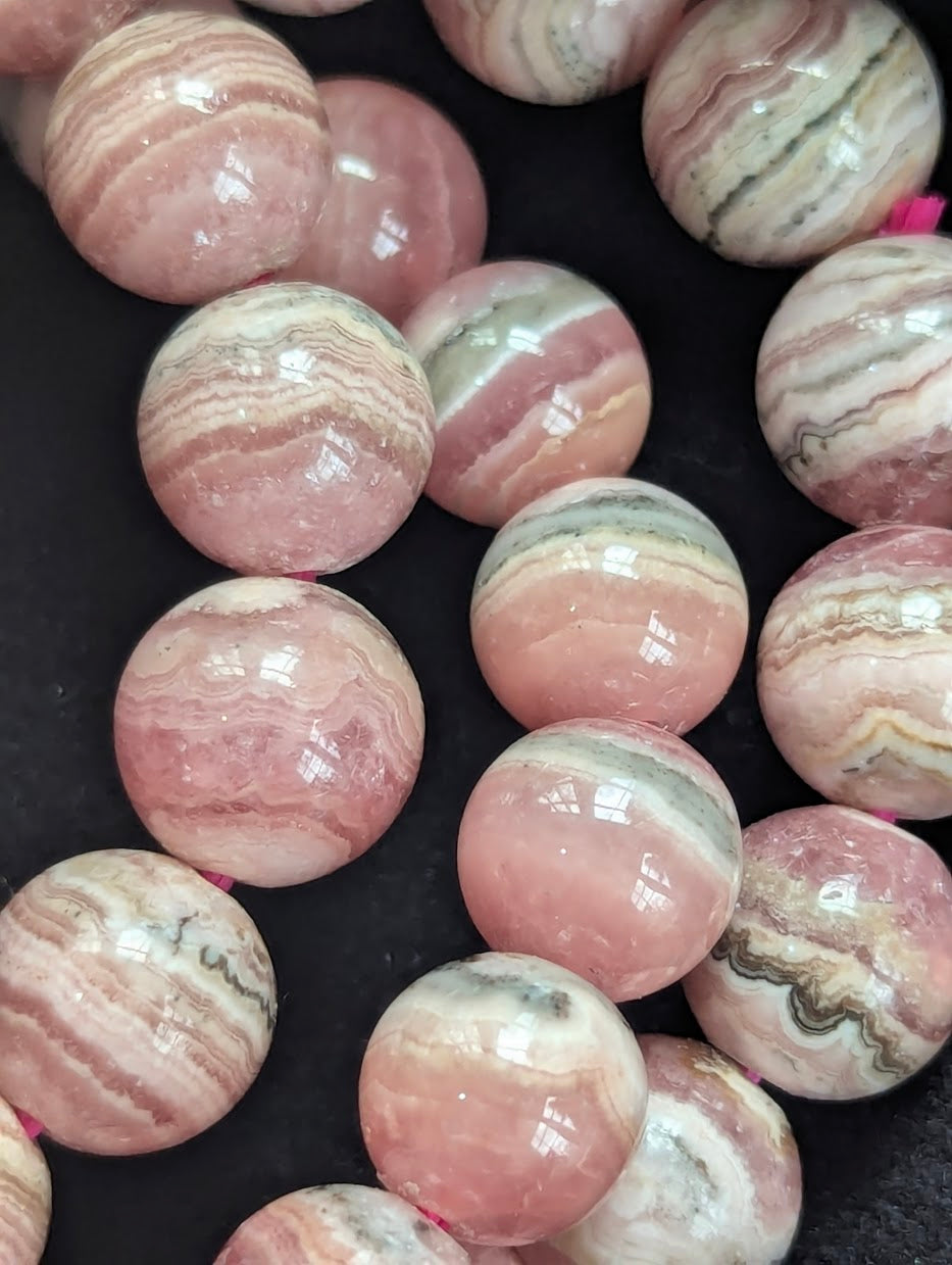 Macro close-up of Argentinian Rhodochrosite beads highlighting distinct stalactitic growth layers and raspberry-pink tones.