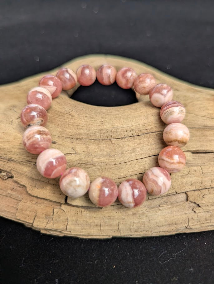 Intuitively selected 11mm polished Argentinian Rhodochrosite beaded stretch bracelet on a driftwood display, showing natural pink and white wavy banding.
