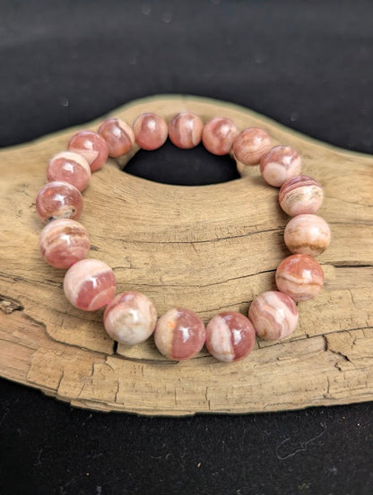 Intuitively selected 11mm polished Argentinian Rhodochrosite beaded stretch bracelet on a driftwood display, showing natural pink and white wavy banding.