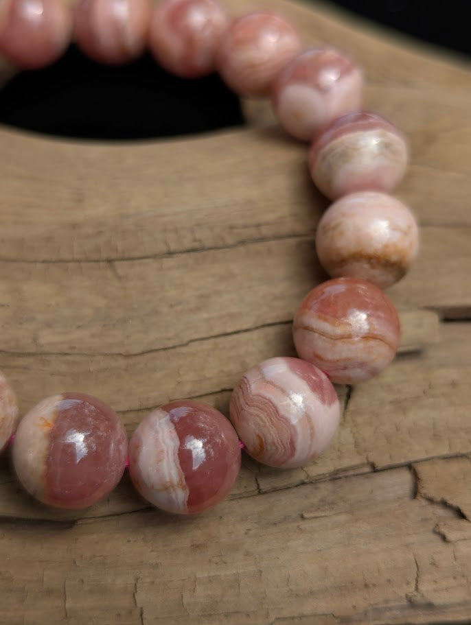 Macro photograph of an 11mm Argentinian Rhodochrosite beaded bracelet showing a high vitreous lustre and intricate pink mineral banding.