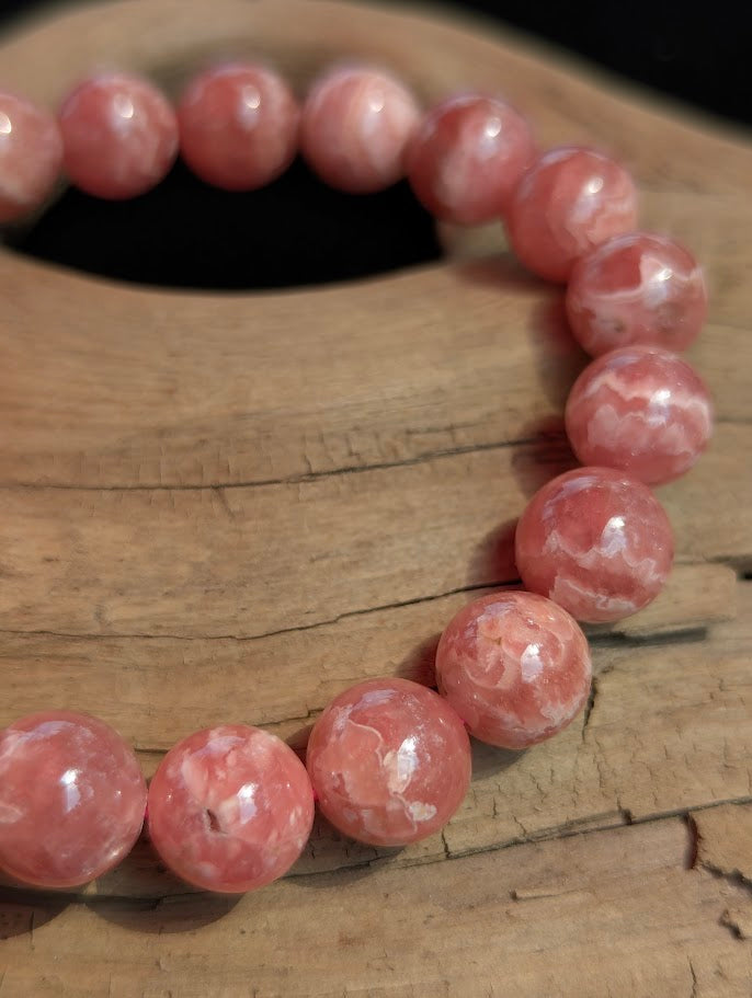 Macro photograph of an 11mm Argentinian Rhodochrosite beaded bracelet showing a high vitreous lustre and intricate pink mineral banding.