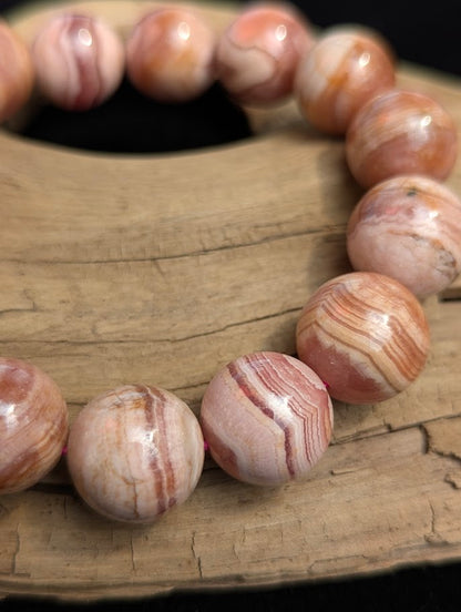 Macro close-up of a 14mm Argentinian Rhodochrosite beaded bracelet highlighting concentric pink and white mineral banding and a pink elastic stretch cord