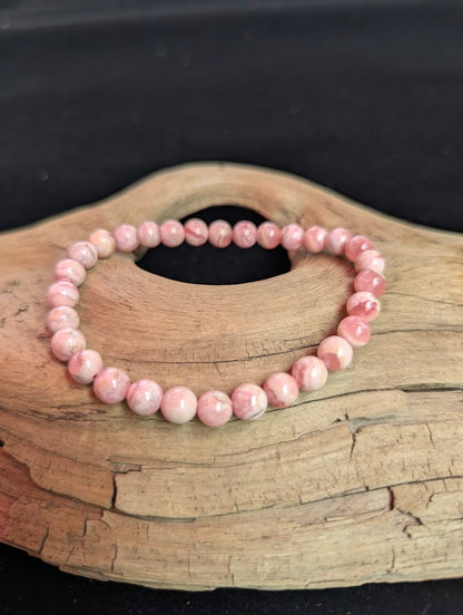 Intuitively selected 6mm polished Argentinian Rhodochrosite beaded stretch bracelet on a driftwood display, showing dainty pink banded stones.