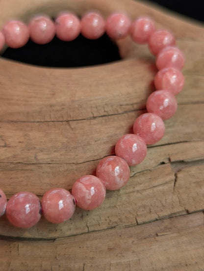 Intuitively selected 7mm polished Argentinian Rhodochrosite beaded stretch bracelet resting on driftwood, showcasing soft pink and white tones.