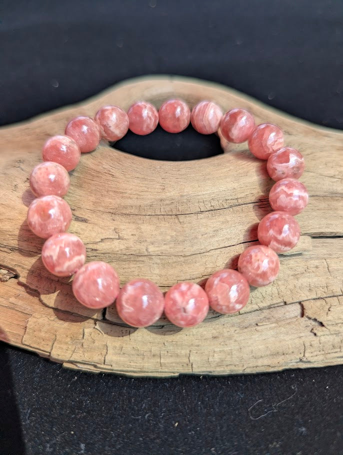 Intuitively selected 11mm polished Argentinian Rhodochrosite beaded stretch bracelet on a driftwood display, showing natural pink and white wavy banding.