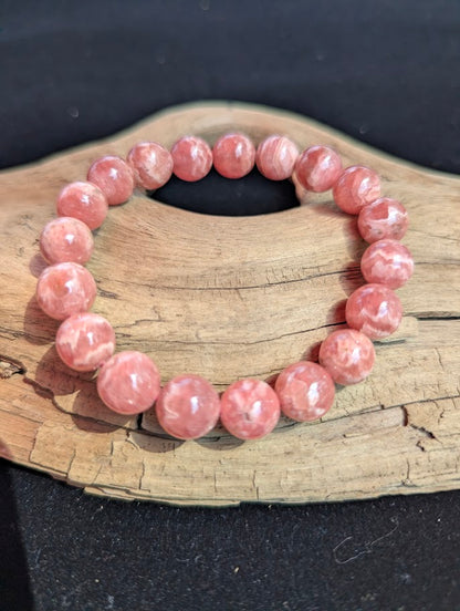 Intuitively selected 11mm polished Argentinian Rhodochrosite beaded stretch bracelet on a driftwood display, showing natural pink and white wavy banding.