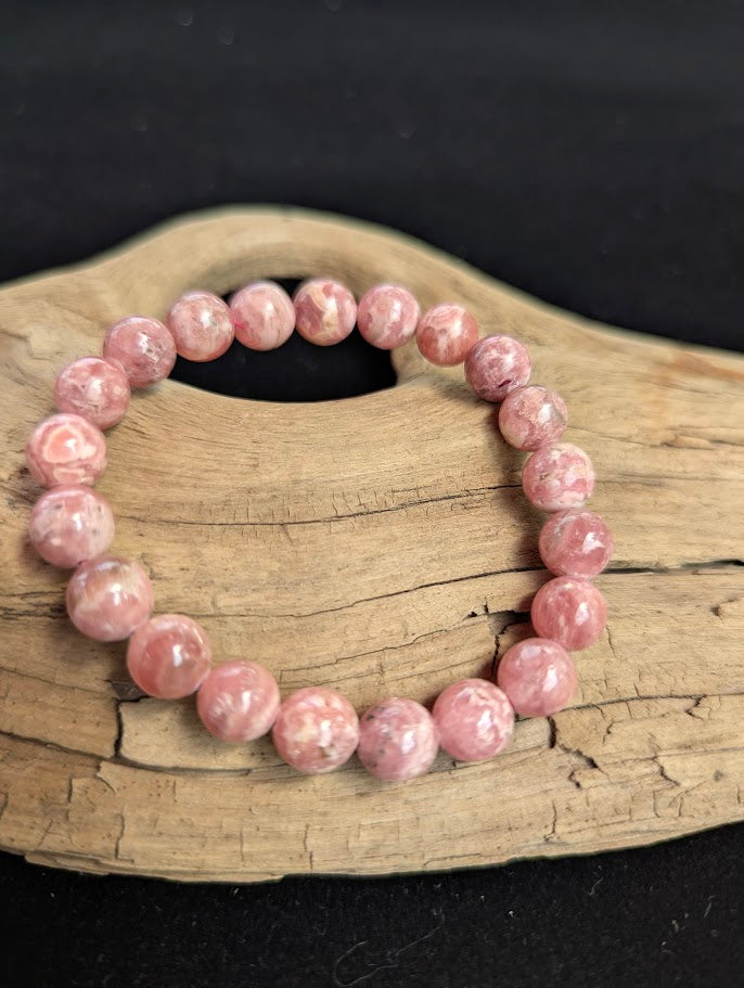 Intuitively selected 9mm polished Argentinian Rhodochrosite beaded stretch bracelet displayed on driftwood, showing uniform pink banded stones.