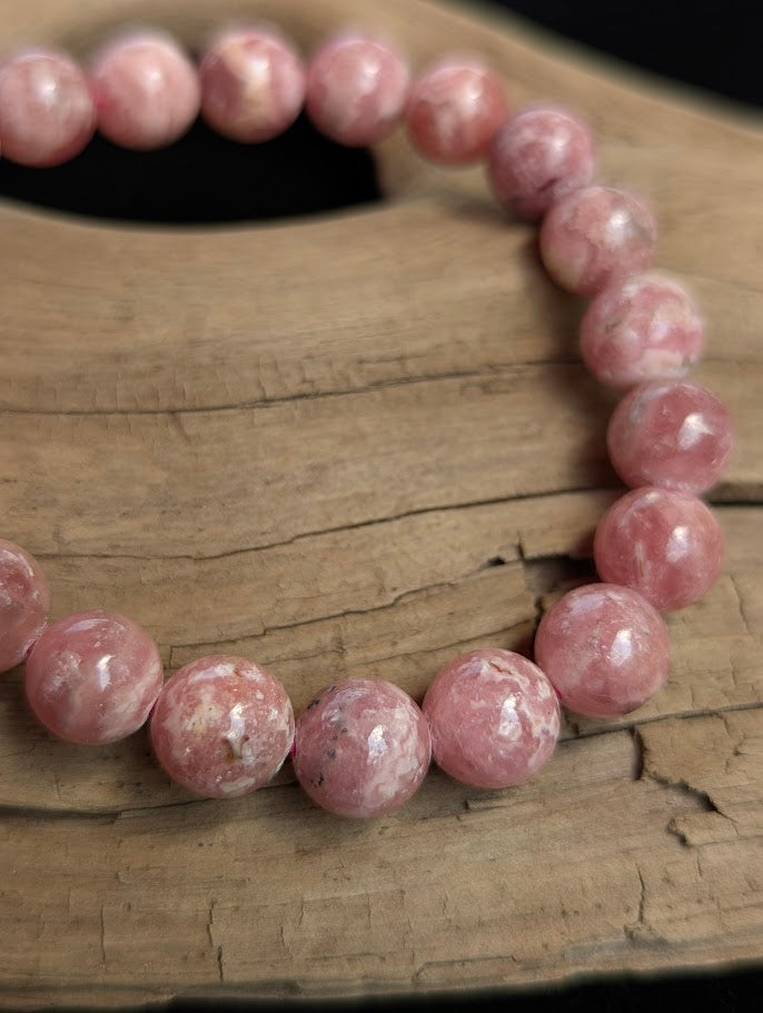 Macro detail of a 9mm Argentinian Rhodochrosite beaded bracelet displaying vibrant rose-pink colouration and distinct white striations.
