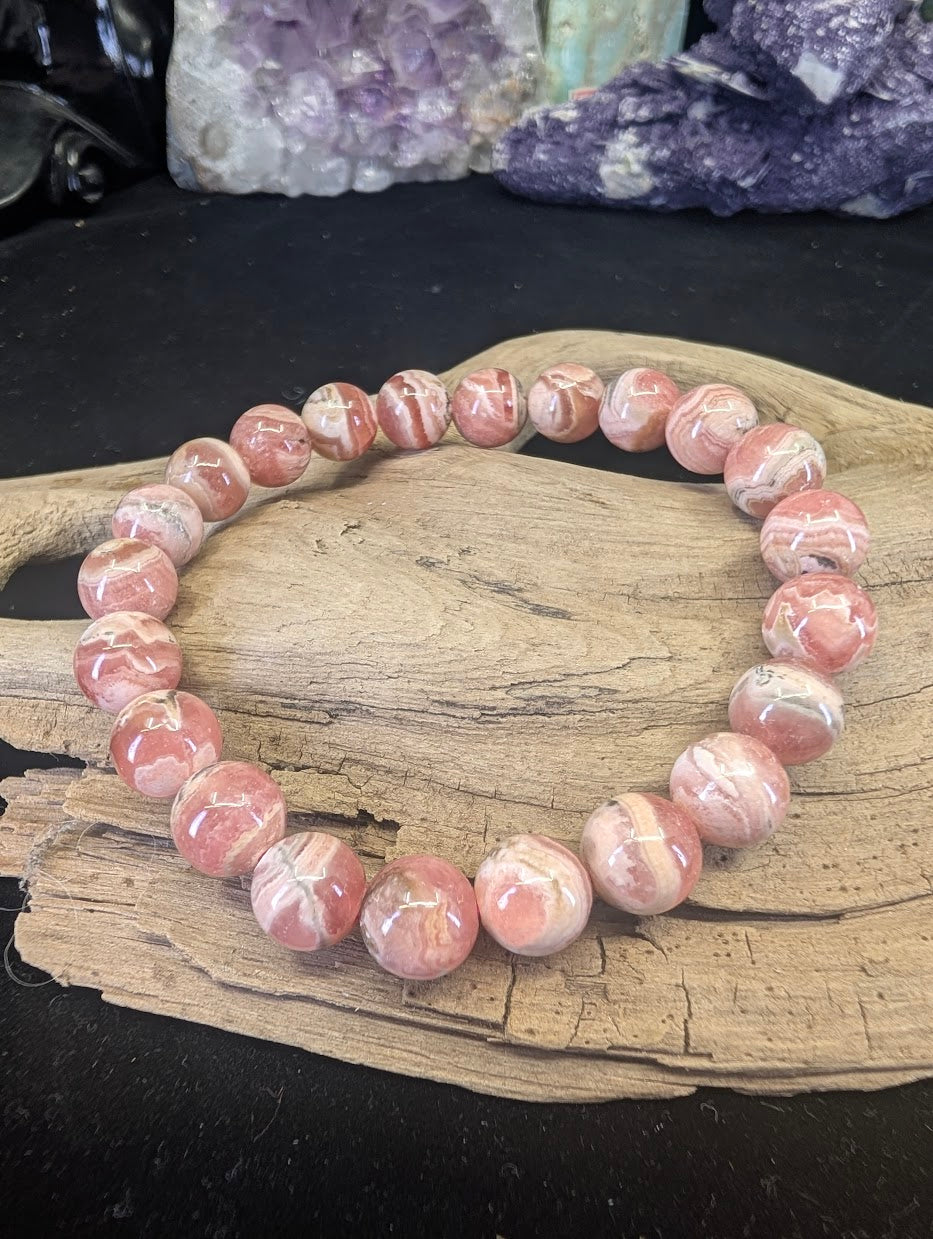 8mm Argentinian Rhodochrosite beaded bracelet displayed on a natural driftwood base showing pink and white banding.