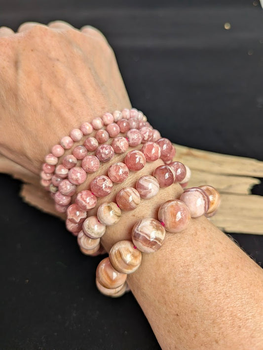 Stack of intuitively selected Argentinian Rhodochrosite beaded bracelets worn together on a wrist, demonstrating size progression from 6mm to 14mm.
