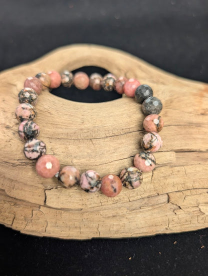 8mm faceted Rhodonite beaded stretch bracelet resting on a driftwood display, showing pink and black contrast.