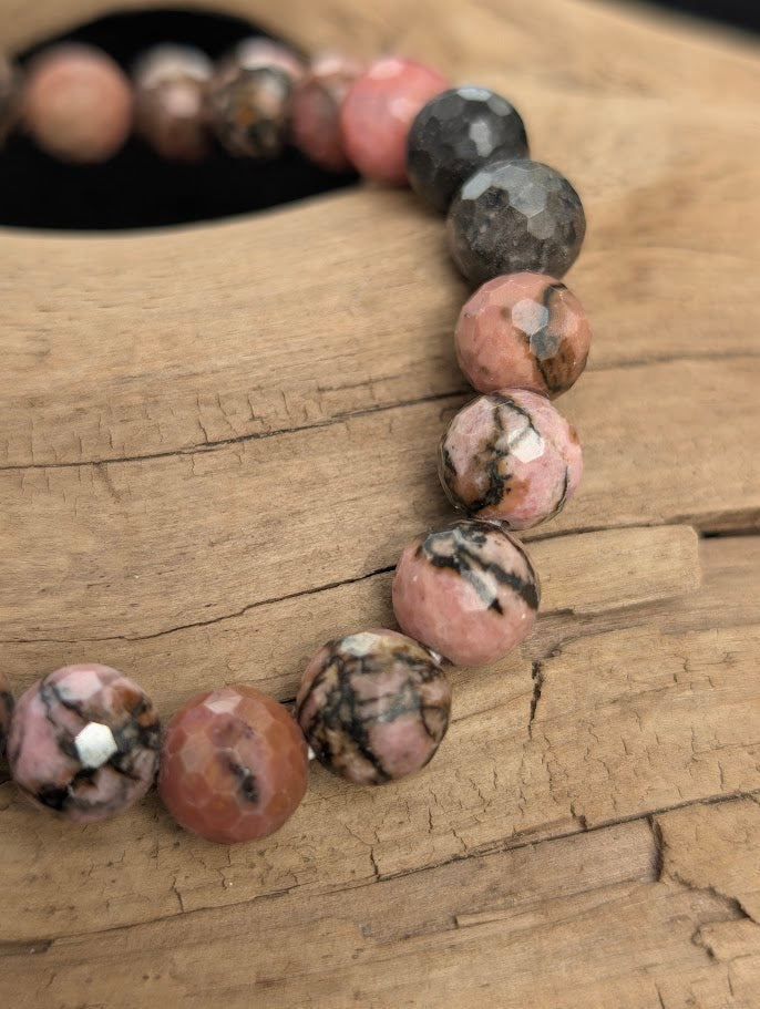 Macro close-up of 8mm faceted Rhodonite beads highlighting geometric surface cuts and black manganese oxide veining.