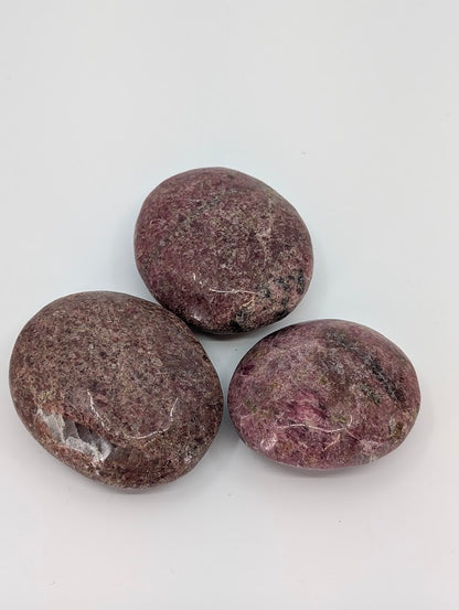 Rhodonite palm stone showing deep rose and plum hues with natural veining, polished surface front view
