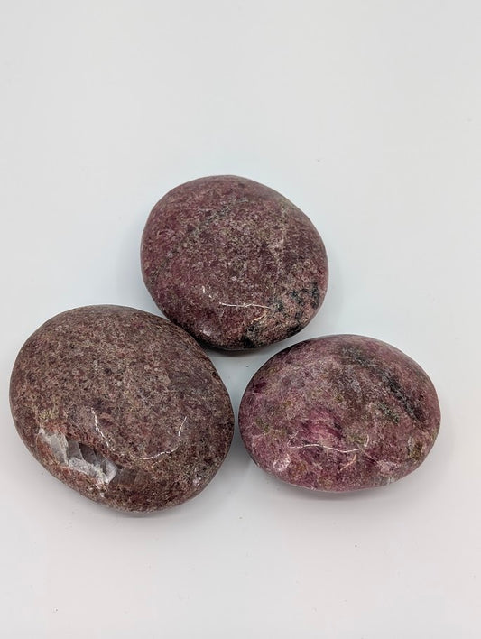 Rhodonite palm stone showing deep rose and plum hues with natural veining, polished surface front view