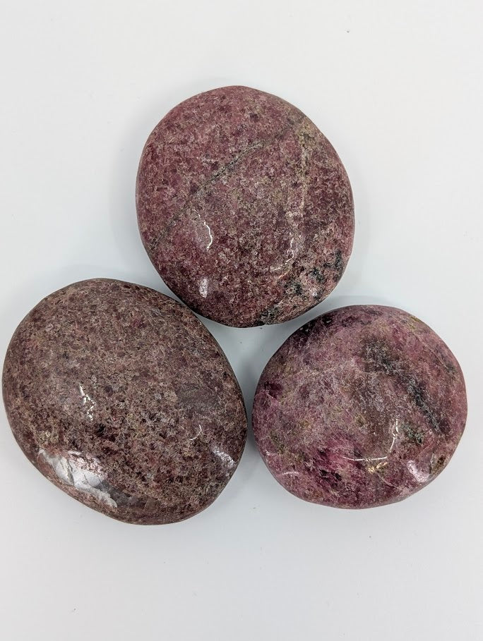 Rhodonite palm stones grouped together with variations of pink, black, and grey mottling