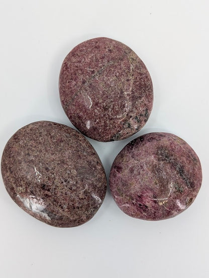 Rhodonite palm stones grouped together with variations of pink, black, and grey mottling