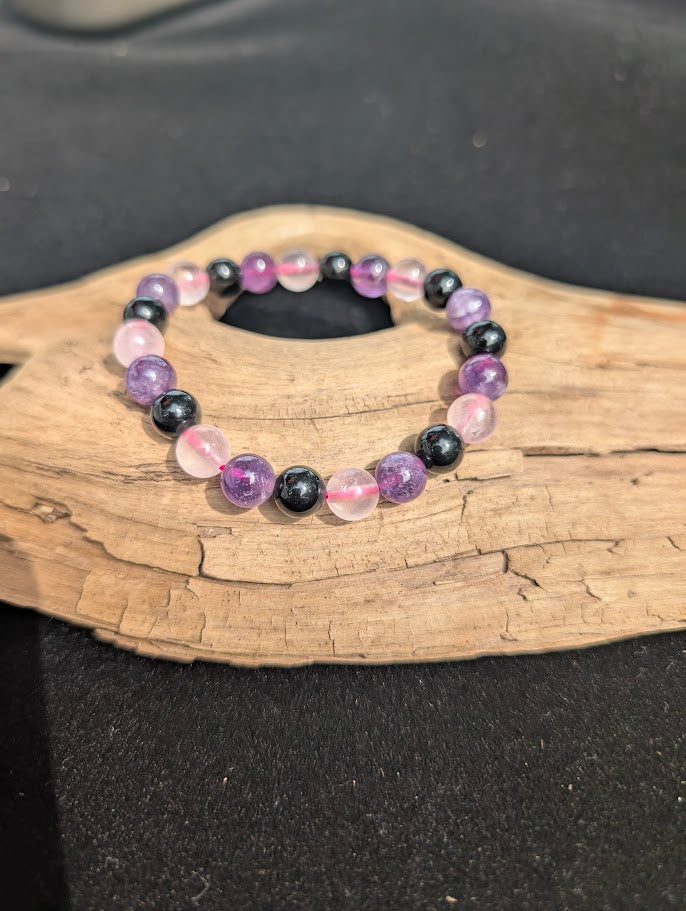 8mm Rose Quartz, Amethyst, and Obsidian beaded bracelet resting on a driftwood display.