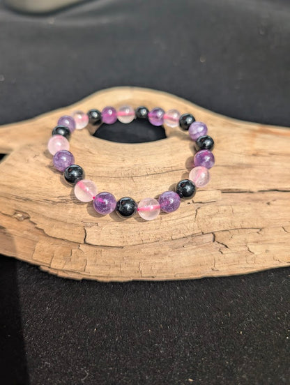 8mm Rose Quartz, Amethyst, and Obsidian beaded bracelet resting on a driftwood display.