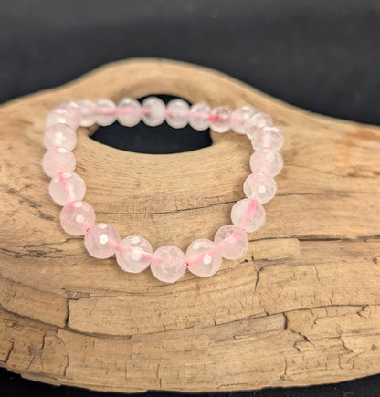 8mm faceted Rose Quartz beaded stretch bracelet resting on a driftwood display, showing soft pink colouration.