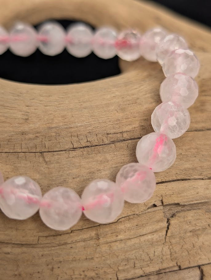 Macro close-up of 8mm faceted Rose Quartz beads highlighting geometric surface cuts and a pink stretch cord.