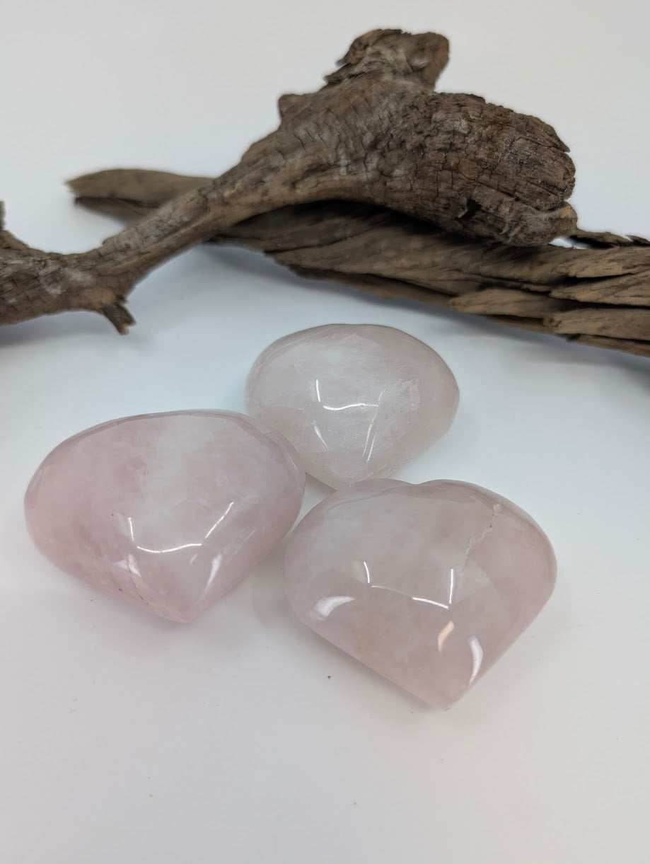 Three polished Rose Quartz puffy hearts on white background with driftwood.