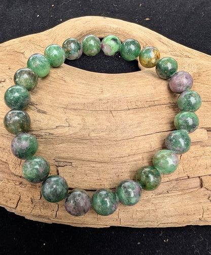 8mm polished Ruby in Fuchsite beaded stretch bracelet resting on a driftwood display, showing green mica and red ruby inclusions.