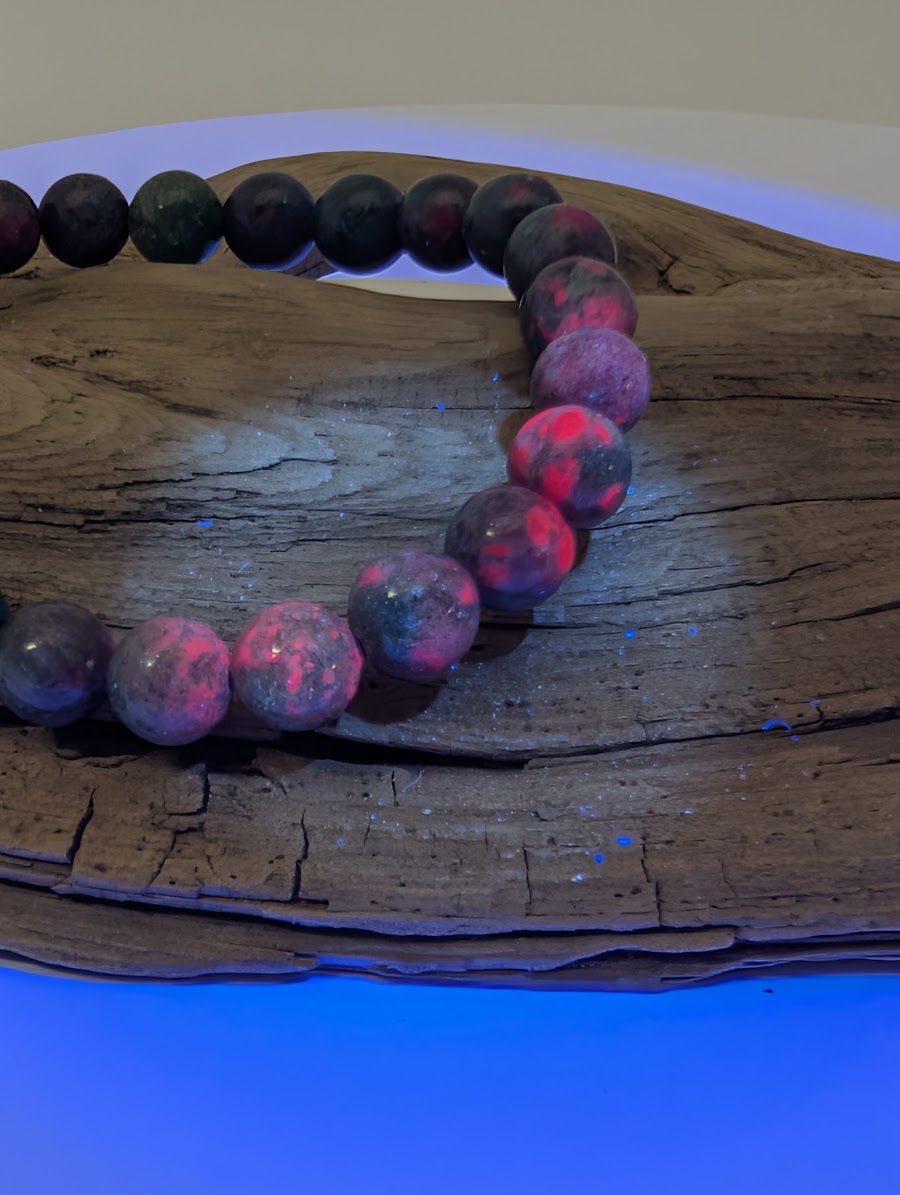 8mm Ruby in Kyanite bracelet under UV light showing vibrant neon-pink fluorescence of natural Ruby crystals.
