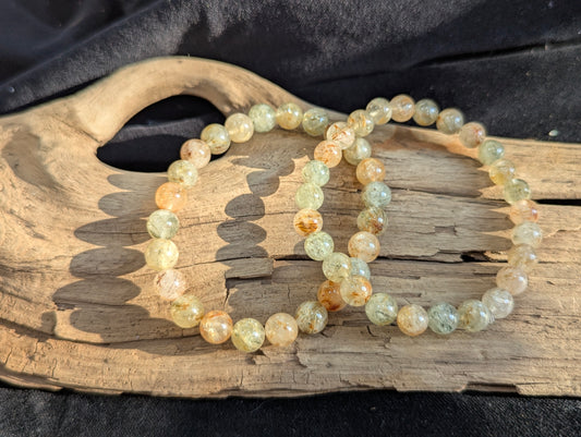 Two 7mm Rutilated Quartz bracelets displayed on natural driftwood.