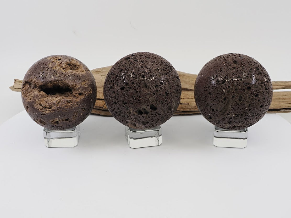 A group of three polished Scoria basaltic lava spheres in reddish-brown tones displayed on clear acrylic stands.