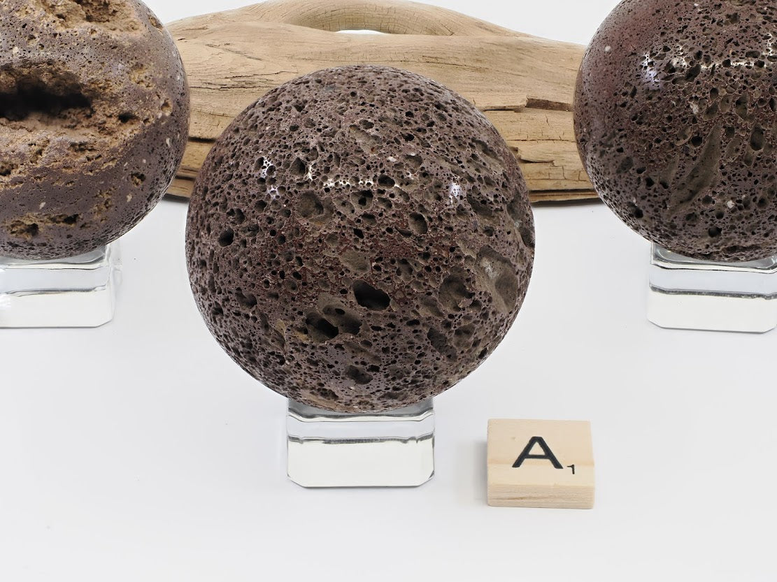 Specimen A: A 57mm polished Scoria lava sphere featuring a fine-pored vesicular texture and deep mahogany color.