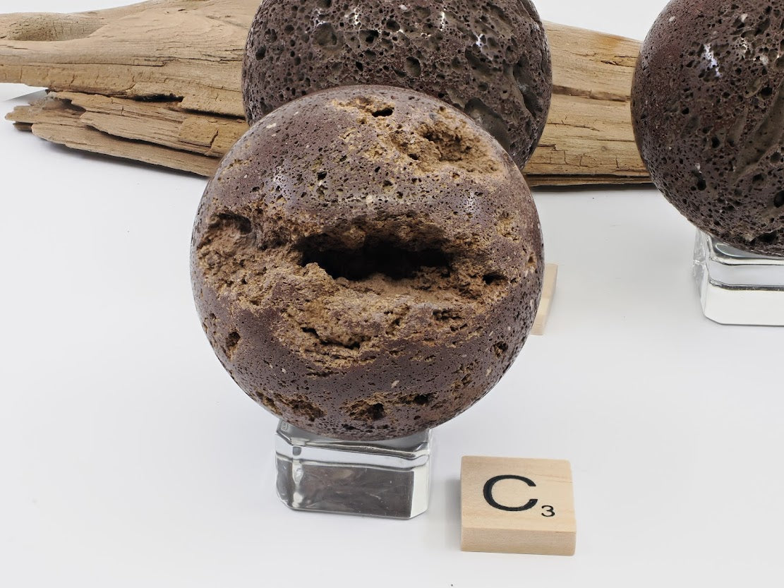 Specimen C: A 55mm Scoria lava sphere featuring a prominent natural vug or cavity revealing raw volcanic texture.
