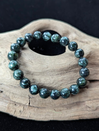 9mm Seraphinite (Clinochlore) Bracelet from Siberia, resting on natural driftwood.