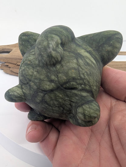 Polished Serpentine Jigglypuff carving held in hand to demonstrate 520g scale and mossy green texture.