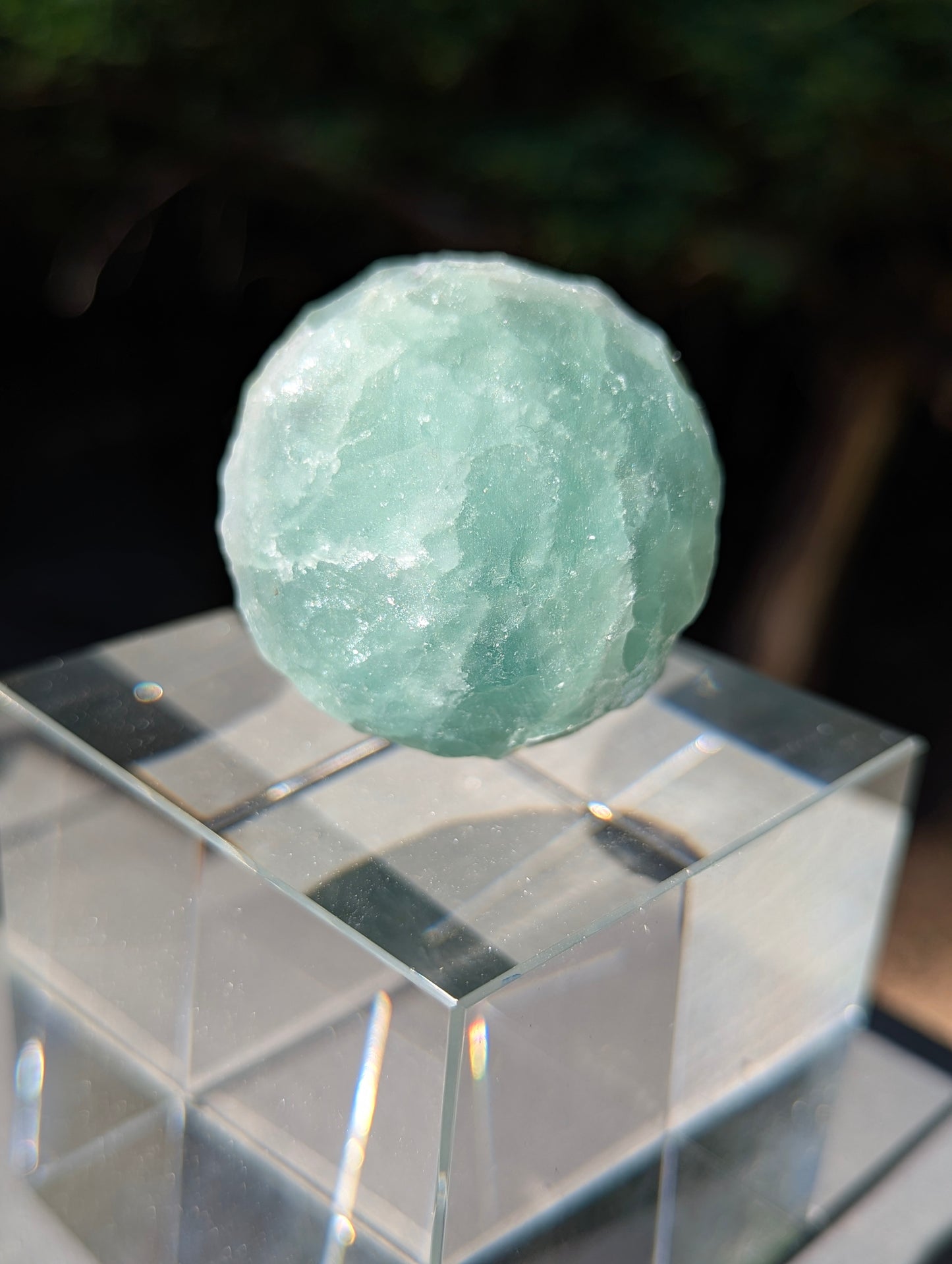 A 50 mm (1.97 in) Silk Fluorite carved moon sphere displaying soft purple and white colour banding on a clear cubic stand.