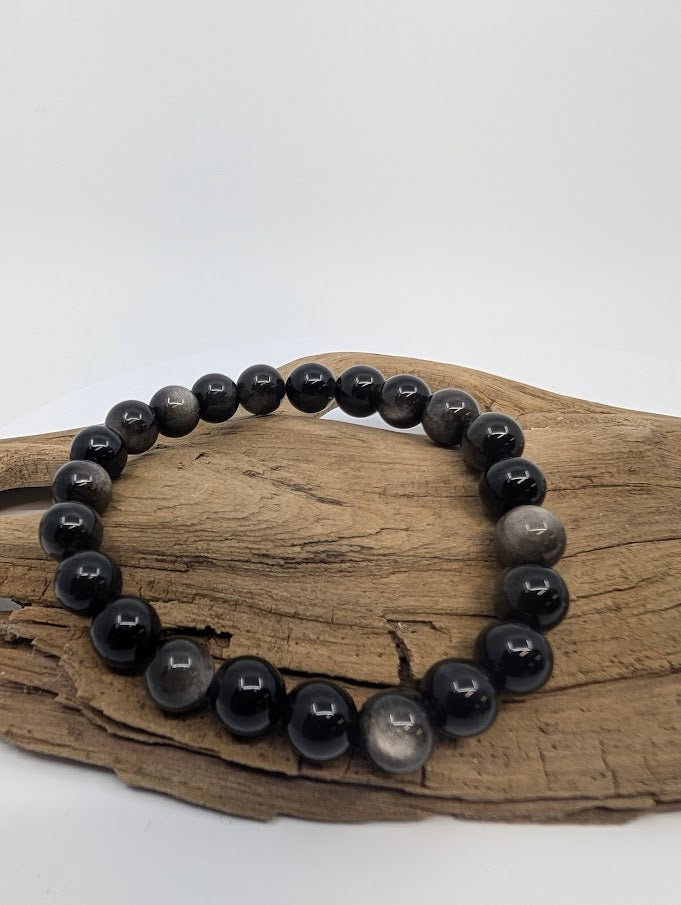 8mm silver sheen obsidian bracelet with glossy black beads displayed on driftwood