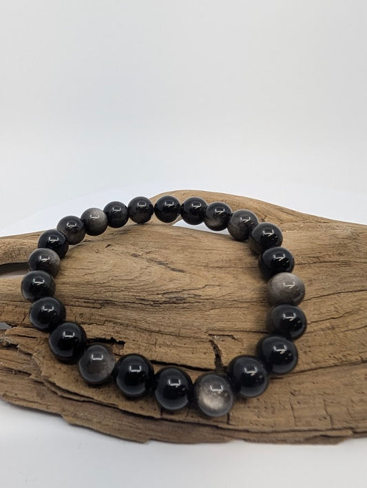 8mm silver sheen obsidian bracelet with glossy black beads displayed on driftwood