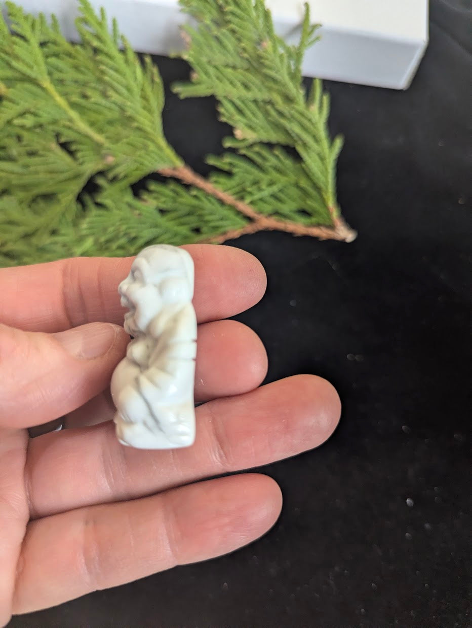 Angled view of a hand-held white Howlite Laughing Buddha carving.