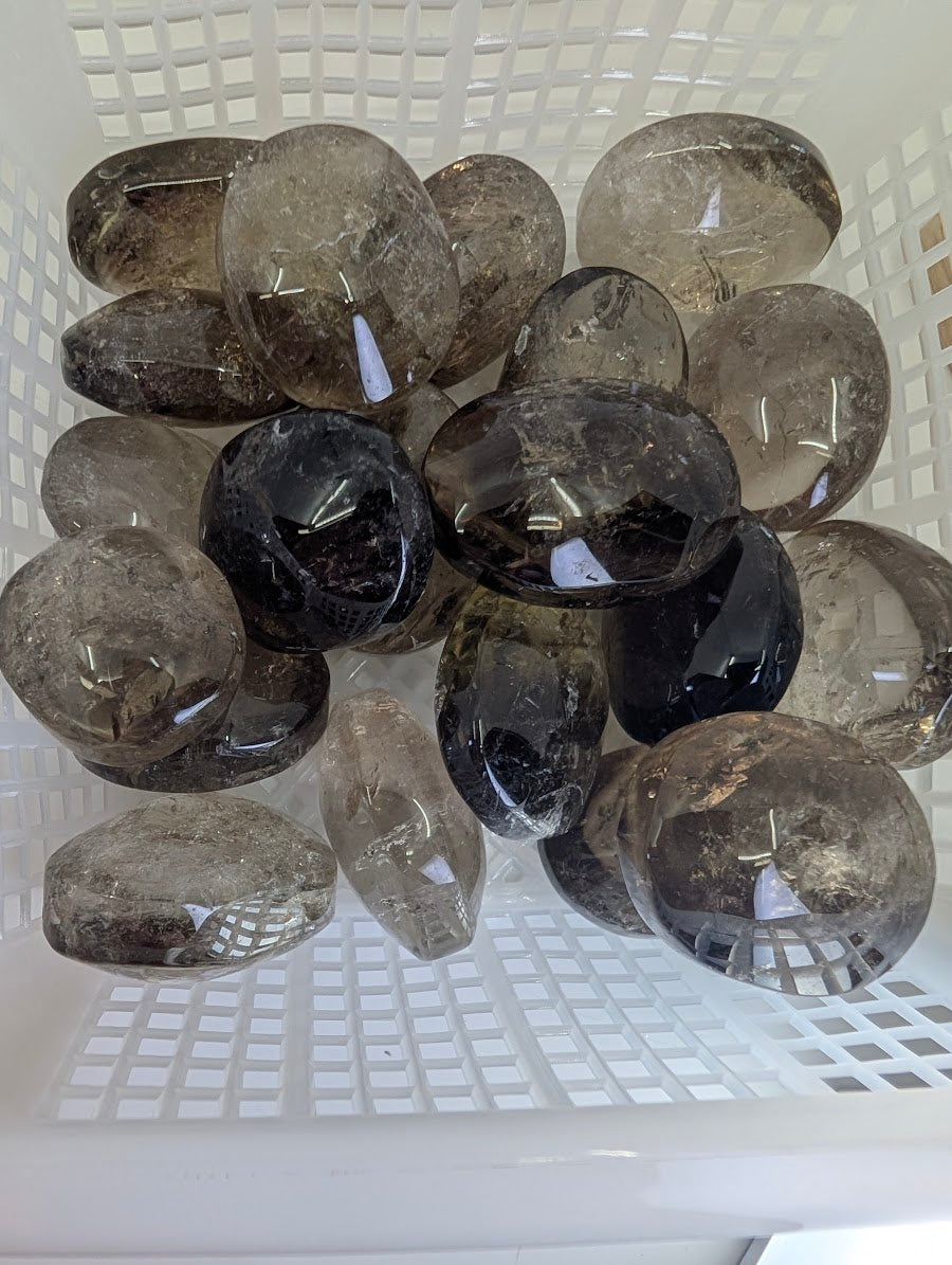 Top-down view of a collection of Lwena Smokey Citrine palm stones in a white sorting basket.
