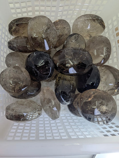 Top-down view of a collection of Lwena Smokey Citrine palm stones in a white sorting basket.