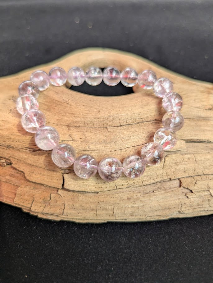 Intuitively selected 10mm AA Grade Smoky Amethyst beaded stretch bracelet resting on driftwood, showcasing high optical clarity.