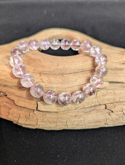 Intuitively selected 10mm AA Grade Smoky Amethyst beaded stretch bracelet resting on driftwood, showcasing high optical clarity.