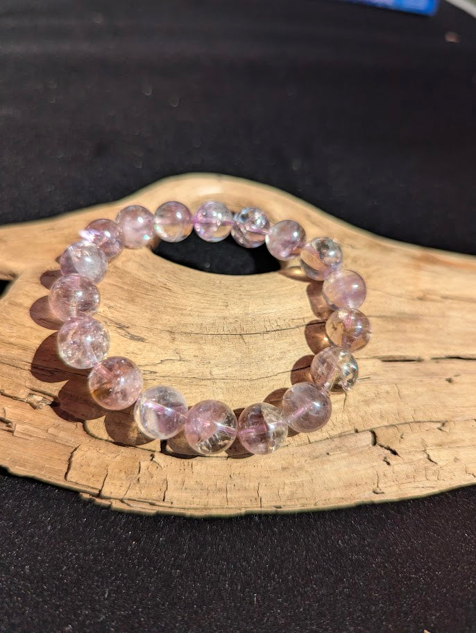 Intuitively selected 11mm AA Grade Smoky Amethyst beaded stretch bracelet displayed on driftwood, showing bi-colour quartz tones.