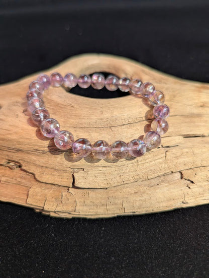 Intuitively selected 8mm AA Grade Smoky Amethyst beaded stretch bracelet on a driftwood display, showing translucent bi-colour quartz and rainbow inclusions.