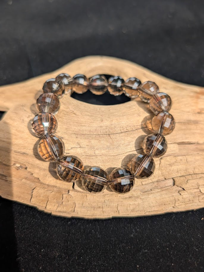 12mm faceted Smoky Quartz beaded stretch bracelet resting on a driftwood display, showing translucent brown clarity.