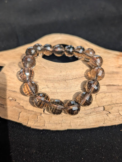 12mm faceted Smoky Quartz beaded stretch bracelet resting on a driftwood display, showing translucent brown clarity.