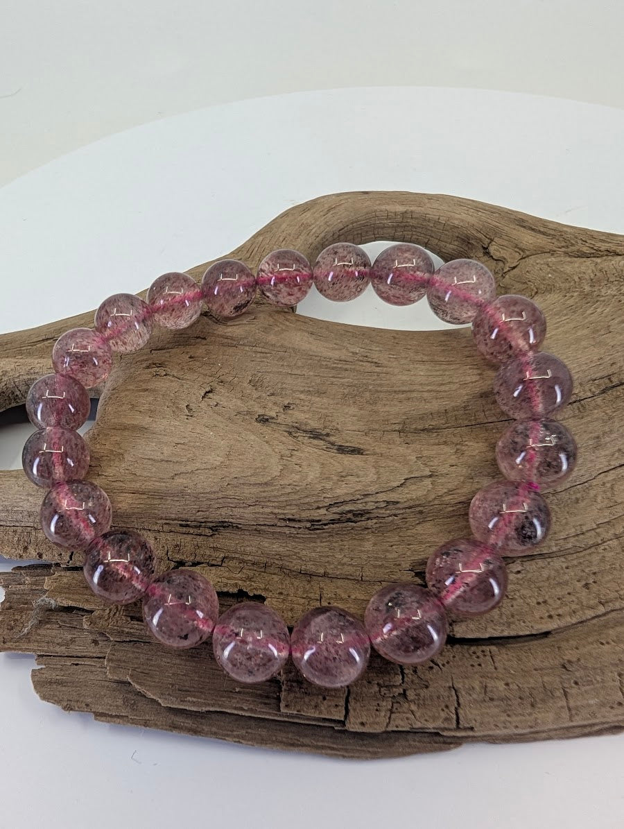 9mm Strawberry Quartz bead bracelet showing natural reddish-pink hematite inclusions on wood.