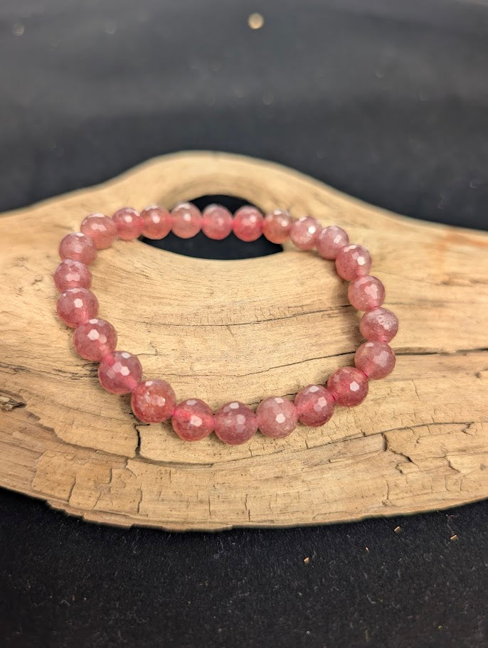 8mm faceted Strawberry Quartz beaded stretch bracelet resting on a driftwood display, showing soft pink colouration.