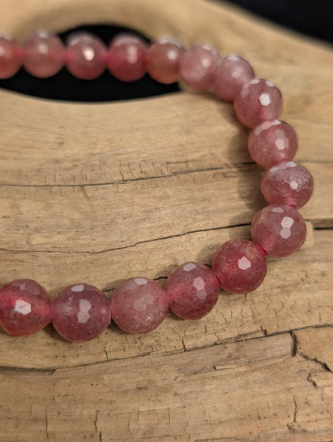 Macro close-up of 8mm faceted Strawberry Quartz beads highlighting geometric surface cuts and a pink stretch cord.
