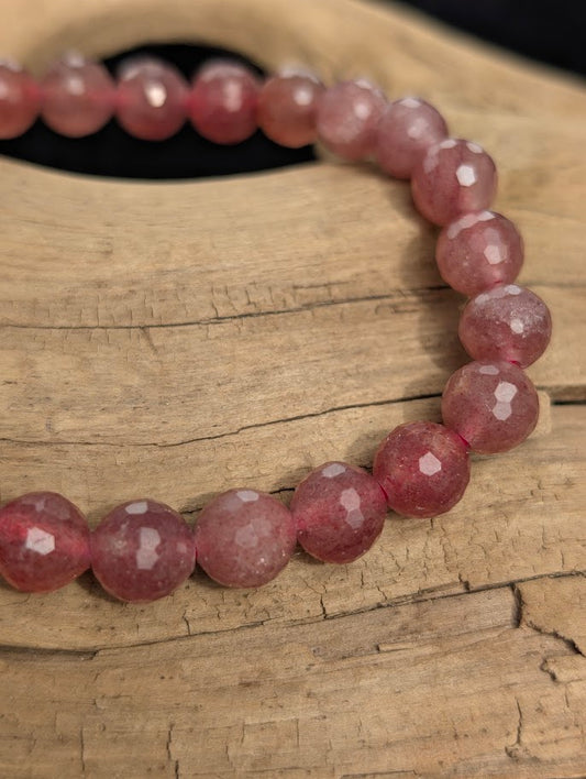 Macro close-up of 8mm faceted Strawberry Quartz beads highlighting geometric surface cuts and a pink stretch cord.